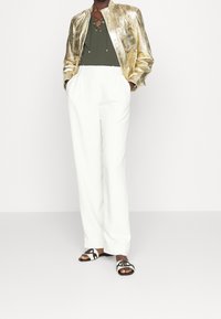 Zlatá metalická bunda se vzorem hadí kůže, olivově zelený top, bílé kalhoty širokého střihu a černobílé sandály na klínku.