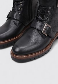 Bottines en cuir noir avec une finition texturée, détail de boucle en métal, bout rond et semelle en caoutchouc avec des crampons profonds.