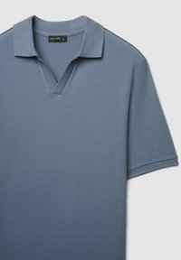 Kurzärmeliges Poloshirt aus strukturiertem hellblauem Stoff, mit V-Ausschnitt und kontrastierendem Kragen. Das Etikett trägt den Schriftzug "CALLIOPE."