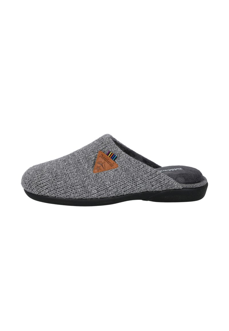 Zapatilla de punto gris con parte superior texturizada, suela de goma negra y una etiqueta triangular marrón con rayas multicolores en el costado.