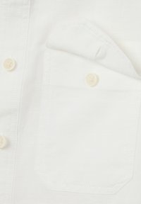 Witte shirt met een zak, gemaakt van lichtgewicht stof. Heeft ronde, witte knopen en zichtbare stiksels, de textuur lijkt glad te zijn.