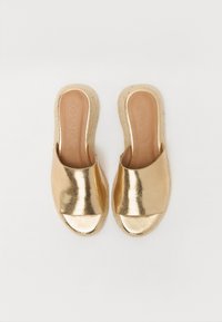 Aukso espadrilės šlepetės su blizgiu metaliniu paviršiumi, atvira nosimi ir natūralia suvyniotų jūtų padais. Lygus paviršius su minimalistiniu dizainu.