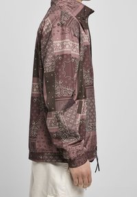 Bunter Windbreaker mit einem burgunderfarbenen und rosa Paisleymuster, hergestellt aus leichtem Material mit elastischen Bündchen und verstellbaren Kordeln.