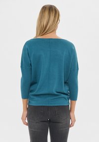 Maglione in teal a maglia con scollo ampio e maniche a tre quarti. Presenta una linea dritta e una texture a coste, con un semplice dettaglio della cucitura posteriore.