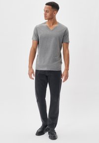 T-shirt grigia in cotone a scollo a V con maniche corte, abbinata a pantaloni neri slim-fit e scarpe nere, mostrata su un modello in piedi.