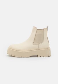Bottines Chelsea en cuir beige avec panneaux latéraux élastiques, semelle à plateforme chunky et accents texturés. Présente une poignée à l'arrière et des détails de couture.