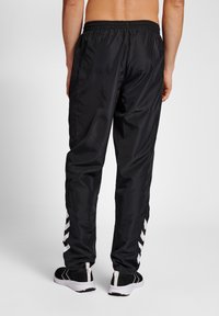 Zwarte nylon sportbroek met een elastische tailleband, voorzien van witte chevrons langs de zijkanten en een comfortabele pasvorm.