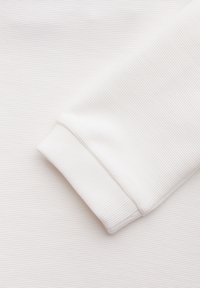 Tela blanca acanalada con una textura suave, presenta un puño doblado y un brillo sutil. Sin patrones visibles ni elementos de hardware.