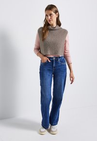 Pull en tricot beige raccourci superposé sur un top à manches longues rose, associé à un jean large bleu et des baskets blanches. Tenue simple et décontractée.