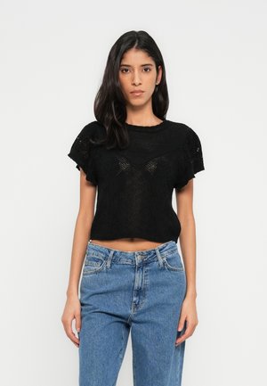 Sort cropped strikket top med korte ærmer, med et tekstureret mønster og bølget halsudskæring, kombineret med højtaljede blå denimjeans.
