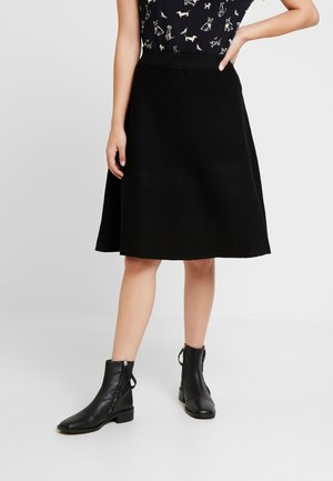 Black A-line skirt made of soft fabric, knee-length, with a fitted waistband. Worn with black ankle boots featuring side zippers.