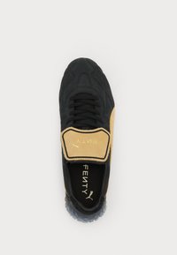 Black sneaker with beige accents, textured upper, lace and strap closure, clear rubber outsole, and "FENTY" logo on the insole.