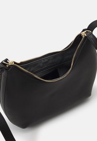 Borsetta in pelle nera con una forma curvata, accentuata da una cerniera dorata e un'unica tracolla. L'interno è foderato in nero e presenta una tasca.