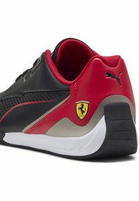 Mustat ja punaiset urheilukengät, joissa on rei'itetty muotoilu, kumipohja, sileä pinta ja metallinen yksityiskohta, jossa on Ferrarin logo.