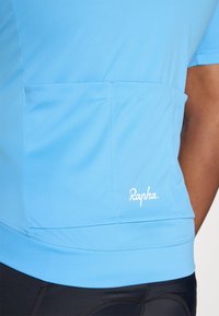 Majica za biciklizam kratkih rukava od svijetloplave tkanine, s stražnjim džepom i bijelim logom "Rapha" na donjoj desnoj strani. Glatka tekstura.