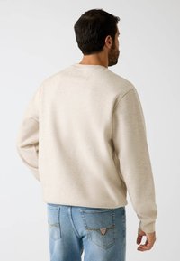 Beige sweatshirts met ronde hals gemaakt van zachte stof, met lange mouwen en een losse pasvorm, gecombineerd met lichte blauwe jeans.