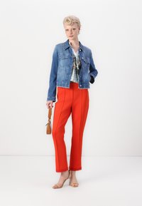 Jeansjacke, cropped Design, in hellblauer Ausführung; kombiniert mit knallroten, taillierten Hosen mit seitlicher Paspelierung und fransigem Saum. Braune Handtasche und Sandalen.