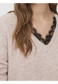 Pull rose clair avec un col en V, orné d'une bordure en dentelle noire autour du col. Texture tricotée, manches longues avec un léger froncé.