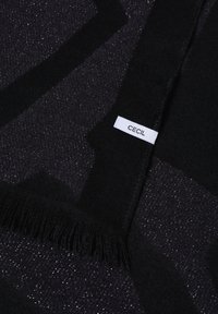 Écharpe noire à franges avec une petite étiquette blanche portant l'inscription "CECIL" posée sur un tissu sombre avec de subtils éclats argentés.