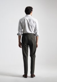 Pantalones verdes de corte ajustado, con bolsillos traseros, una textura suave y puños enrollados, combinados con una camisa de rayas verticales.