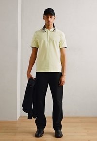 Bledosivá polo tričko s čiernymi detailami, čierne nohavice, v ruke tmavá bunda, na hlave čierna čiapka a čierne topánky. Jednoduchý, neformálny outfit.