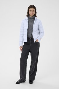 Helle blaue gesteppte Jacke mit Reißverschluss, getragen über einem grauen Rollkragenpullover und einer schwarzen weiten Hose, die ein dezentes Logodetail aufweist.