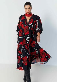 Zwarte jurk met rood bloemenmotief, voorzien van een V-hals, pofmouwen, een gelaagde rok en een opvallend patroon tegen een witte achtergrond.