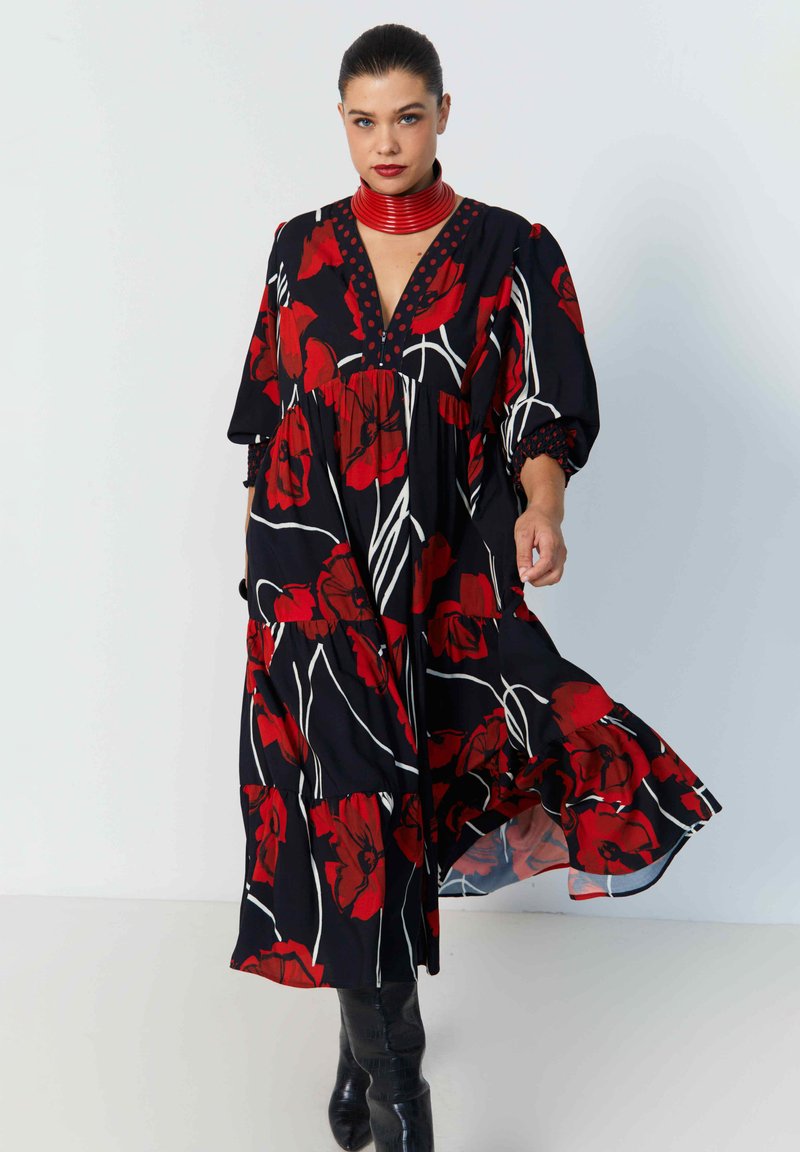 Zwarte jurk met rood bloemenmotief, voorzien van een V-hals, pofmouwen, een gelaagde rok en een opvallend patroon tegen een witte achtergrond.