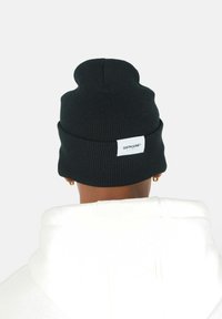 Svart ribbad stickad mössa med uppvikt kant och en liten vit etikett med "SIXTH JUNE." Mot en enfärgad vit bakgrund.