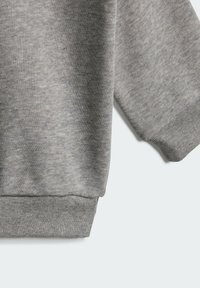 Tessuto grigio di felpa con un motivo di maglia testurizzata, caratterizzato da polsini e orlo a costine. La manica si estende parzialmente all'interno del fotogramma.