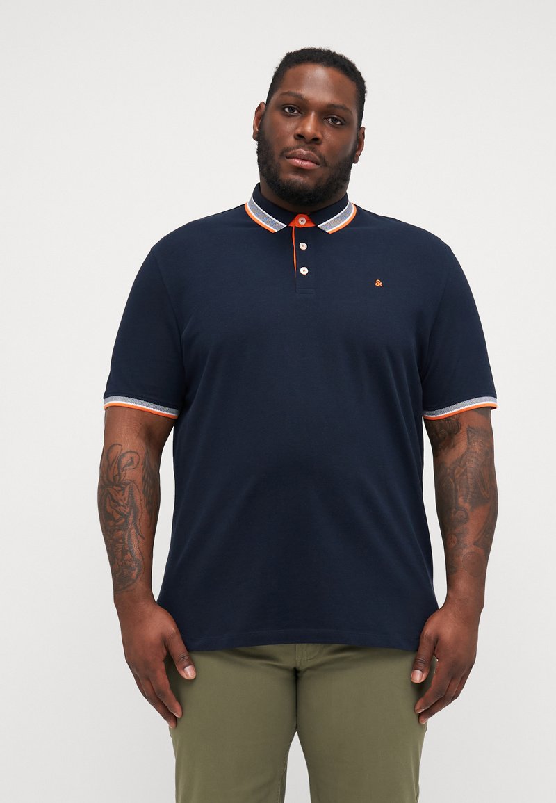 Marineblå poloskjorte laget av bomull med brodert logo. Har en kontrasterende krage og ermetrems i oransje og grått. Klassisk passform.