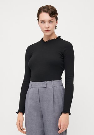 Czarny longsleeve z teksturowanym falbaniastym dekoltem, w zestawie z jasnoszarymi spodniami z wysokim stanem, z wyraźnymi kantami i bocznymi kieszeniami.