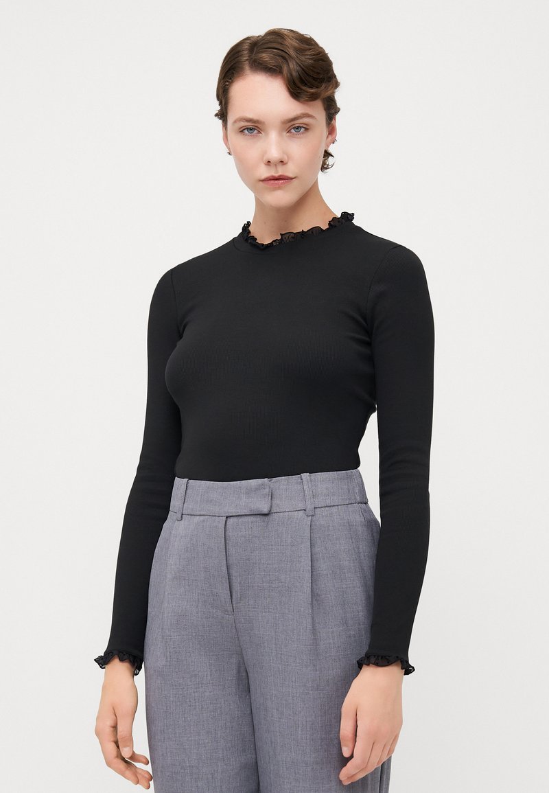 Black long-sleeve top with a textured ruffled neckline, paired with light gray high-waisted trousers featuring sharp creases and side pockets.