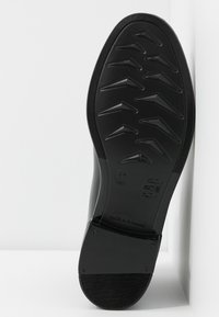 Semelle d'une chaussure noire avec des motifs angulaires, taille 37, et "Fabriqué en Roumanie" embossé sur la zone du talon.