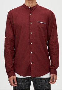 Chemise bordeaux à manches longues avec col officier, dotée d'une poche poitrine discrète, d'une patte de boutonnage et de boutons blancs contrastants.