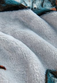 Tela suave de rizo en un tono gris claro con textura en primer plano y ligeros pliegues, mostrando matices de patrones azules y marrones a lo largo de los bordes.