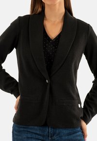 Zwarte gebreide blazer met een op maat gemaakte silhouet, gesneden revers, enkele knoopsluiting en twee voorzakken, gedragen over een polkadot top.