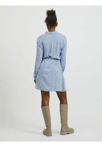 Blå skjortklänning med krage, långa ärmar och knyt i midjan, med ett prickigt mönster. Matchad med knähöga beige stövlar.