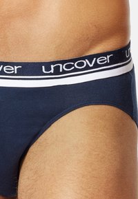 Marineblaue Baumwollunterhose mit weiß gestreiftem Elastikbund. Verfügt über eine weiche Textur und ein figurbetontes Design, das den Beinausschnitt und die Markenlogo am Bund betont.