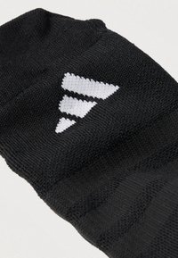 Fekete sportzokni texturált anyagból, fehér geometriai logóval. A zokni szoros illeszkedésű és bordázott szegélyű a kényelemért.