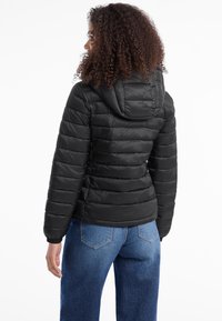 Svart dunjakke med horisontal quilting, hette og elastiske mansjetter, kombinert med blå denimjeans. Enkelt design og matt finish.
