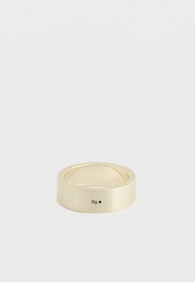 Guldfarvet ring af bånd med en mat finish, afrundede kanter og indgraveret markering "9g" på overfladen, rektangulær form, glat tekstur.