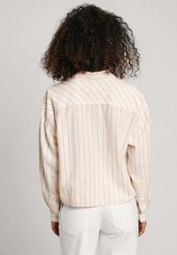 Striped button-up shirt with vertical orange and white stripes, relaxed fit, long sleeves, and a curved hem. Soft fabric texture.
