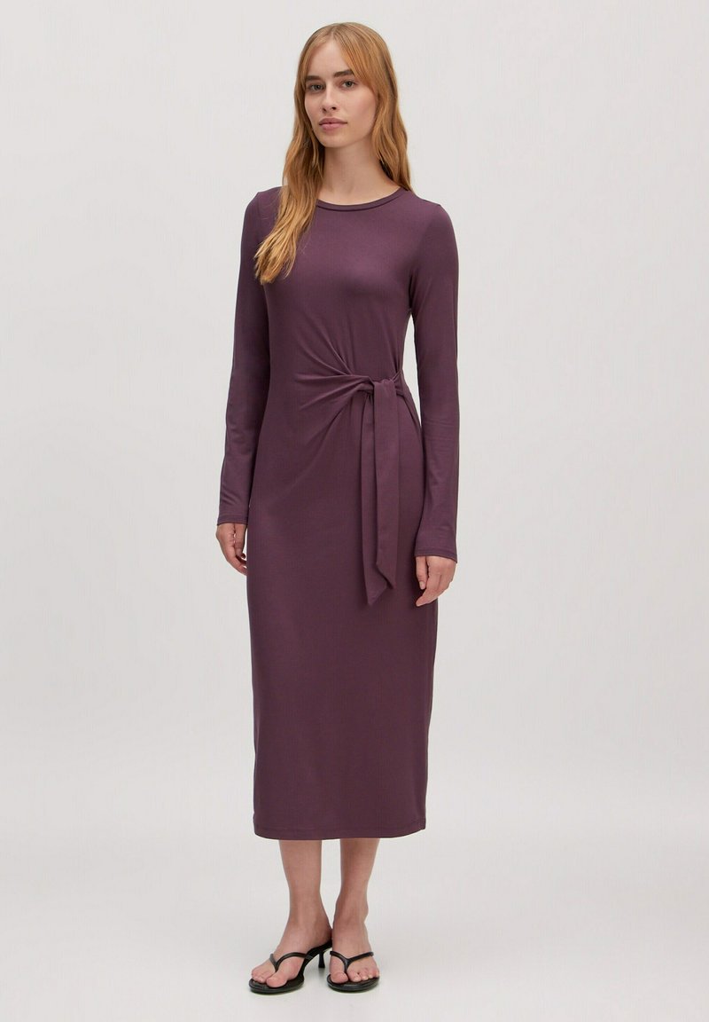 Robe longue mauve à manches longues avec un détail de taille nouée, faite d'un matériau doux et extensible. Longueur au sol avec un col rond.