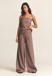 Rjavi top brez naramnic v kombinaciji z ujemajočimi širokimi hlačami iz teksturirane tkanine. Obleka ima sproščen kroj in subtilno drapiranje.