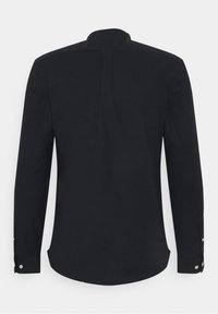 Camisa negra de manga larga con cuello alto, que presenta un yugo trasero, aberturas laterales y puños abotonados. Textura suave y corte entallado.