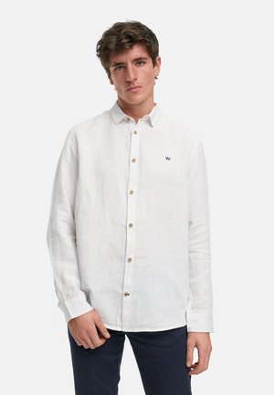 Witte linnen overhemd met lange mouwen, een knoopsluiting aan de voorkant, bruine knopen en een klein marineblauw geborduurd logo op de borst.