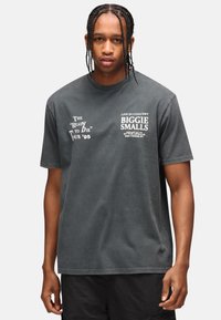 Šedé bavlněné tričko s bílým grafickým textem. Text obsahuje "Ready to Die Tour '95" a "Biggie Smalls". Krátké rukávy, design s kulatým výstřihem.