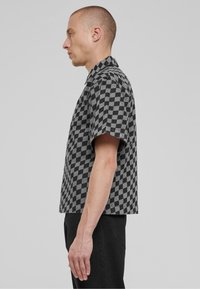 Camisa de manga corta con cuello que presenta un patrón de tablero de ajedrez en blanco y negro. Fabricada con un material texturizado y un corte relajado.