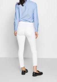 Jeans ajustados blancos, mezcla de algodón con una textura suave. Combinados con una camisa de botones azul claro. Zapatos negros sin cordones con un detalle de hebilla.